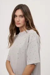 Remera oversized de manga corta y cuello redondo, de color negro con efecto acid wash y aplicación de strass en la parte superior.