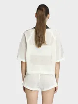 Polo de crochet color blanco con cuello polo negro en V, mangas cortas con las icónicas tres tiras de Adidas en negro y logo de la marca bordado en el pecho.