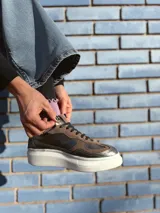 Zapatillas deportivas de cuero color peltre, con cordones negros y suela de goma blanca.