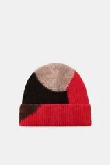 Gorro tipo beanie de punto con diseño de bloques de color en tonos rojo, negro y beige. Presenta un acabado con vuelta y textura suave.