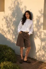 Camisa blanca de silueta relajada, con cuello alto abotonado, cartera frontal y mangas largas con puños amplios. Presenta terminación elastizada que genera un sutil efecto abuchonado.