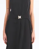 Vestido largo negro sin mangas, con cuello redondo, corte holgado y abertura lateral en la falda. Presenta un cinturón con hebilla metálica plateada.