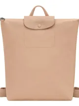 Mochila de diseño minimalista en color beige, con cierre superior de cremallera y solapa frontal con botón a presión. Presenta un asa superior y correas ajustables, con el logo de la marca grabado en la solapa.