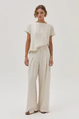 Pantalón de lino color beige, de pierna ancha, con botón en la cintura, pinzas en el frente y bolsillos delanteros y traseros.