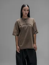 Remera de manga corta con diseño oversize, confeccionada en algodón con proceso batik artesanal en tono óxido. Presenta recortes superpuestos en el frente y costuras expuestas en mangas y cuerpo.