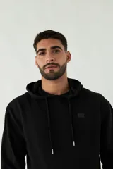 Buzo de felpa negro con capucha, cordones ajustables y bolsillo tipo canguro. Tiene puños y cintura acanalados, y logo en grifa de plástico.