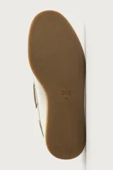 Mocasines tipo náutico de piel en color blanco, con suela plana de goma marrón, cordones y ojalillos metálicos laterales.