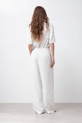 Pantalón de lino color blanco con finas rayas verticales negras, corte palazzo, cintura alta con pinzas y cinturón marrón.