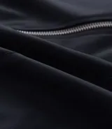 Campera masculina de corte boxy en color beige, con cuello inglés, cierre frontal de cremallera, mangas largas con puños elásticos y ruedo con elástico. Presenta bolsillos laterales y detalles de recortes en el diseño.