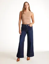 Jean wide leg azul oscuro de tiro alto, con pierna ancha y ruedo con tajo lateral. Presenta pretina con pasadores, botón y cierre, y bolsillos delanteros y traseros.