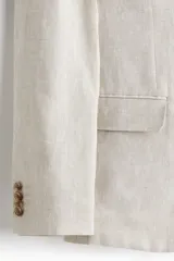 Blazer de lino liviano color beige, con solapas de muesca finas, botonadura sencilla de un botón, bolsillos con solapa en el frente y bolsillo superior ojal.