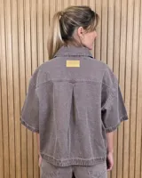 Sobrecamisa de denim soft color beige, con cuello camisero, mangas cortas amplias, bolsillos frontales con solapa y cierre de botones metálicos.