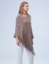 Poncho tejido en hilo soft, con efecto jaspeado multicolor (predominantemente tonos oscuros como azul marino, negro, y toques de violeta y dorado/lurex). Presenta un diseño asimétrico y flecos largos en los bordes.