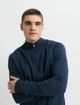 Cardigan de punto color azul, con cuello alto y cierre frontal completo. Presenta mangas largas tipo ranglan y puños acanalados.