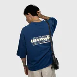 Remera de corte oversize color azul, con estampa gráfica en la espalda que incluye texto y diseño lineal.