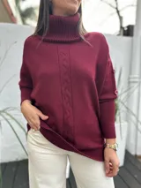 Polerón de cuello alto en color bordó, con diseño de tejido trenzado vertical en el centro y detalle de botones en las mangas. Presenta puños y ruedo acanalados.