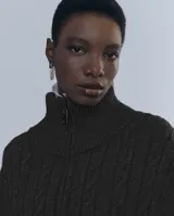 Chaleco largo de punto trenzado color gris con cuello alto y cierre frontal con cremallera metálica.