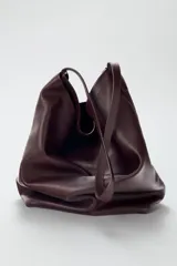 Bolso formato saca color marrón oscuro, confeccionado en piel. Tiene doble compartimento interior, asa de hombro y bolsillo interior con cierre mediante cremallera.
