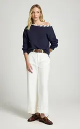 Sweater azul marino de tejido de punto con escote barco, detalle contrastante en color blanco a lo largo del borde, mangas largas con hombros caídos y ajuste ligeramente holgado.