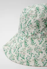 Gorro tipo bucket hat estampado con flores y hojas en tonos verde y celeste sobre fondo blanco. Es reversible.