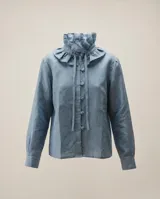 Camisa de lino celeste con cuello alto con volado y lazo, manga larga con puños abotonados y botones forrados a tono en el frente.