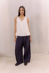 Musculosa blanca de diseño holgado con escote en V, costuras decorativas frontales, tablas encontradas en el centro y un delicado volado en el ruedo.