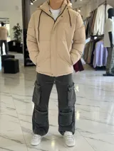 Campera puffer impermeable color beige con capucha desmontable con cordones negros, cierre frontal con cremallera y solapa con botones a presión.