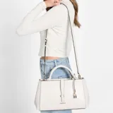 Cartera Guess modelo Carrie de color blanco, confeccionada en símil cuero con herrajes dorados. Presenta doble asa de mano, correa ajustable y desmontable, y detalle de candado colgante. Incluye el logo de la marca en la parte frontal.