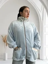 Campera celeste de tela tipo peluche, con cierre frontal, cuello alto y bolsillos con ribete plateado.