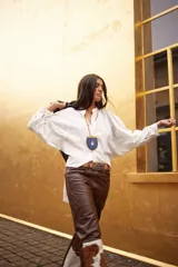 Camisa de lino blanca, de corte oversize, con mangas largas abullonadas, cuello mao y botones. Es más larga en la parte trasera e incluye un tajo en la espalda.