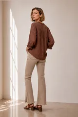 Blusa de manga larga color marrón, con cuello redondo y detalles fruncidos con volados pequeños en el cuello y los puños. Presenta cierre frontal con pequeños botones blancos y delicados pliegues verticales en el pecho.