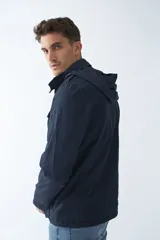 Campera de gabardina verde militar con capucha desmontable y ajustable, cierre frontal con cremallera y múltiples bolsillos con solapa.