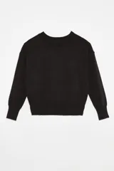 Sweater tejido color marrón claro, de escote redondo y calce holgado. Tiene hombros caídos, mangas largas y puños tejidos.