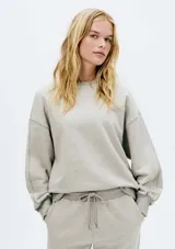 Buzo de tejido de punto color gris melange, con cuello redondo y corte holgado. Presenta costuras visibles en los hombros y puños y cintura acanalados.