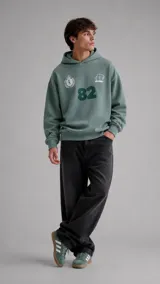 Hoodie verde con capucha, diseño de estampado frontal con el número 82, un escudo y el logo de la marca Duxon. Presenta puños y ruedo acanalados.