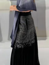 Falda larga plisada color marrón con estampado geométrico dorado en la parte superior y bolsillos laterales.