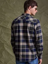 Camisa de manga larga en color azul noche con un patrón de cuadros finos en tonos rojos y verdes. Presenta cuello clásico, cierre frontal con botones y un bolsillo en el pecho con solapa.