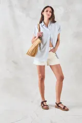 Blusa de viscosa rayada en blanco y celeste, con cuello camisero, mangas cortas con dobladillo y botones frontales.