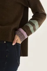 Sweater tejido de lambswool color beige, con cuello redondo y puños acampanados con rayas de colores (marrón, mostaza, bordó y beige). Incluye un detalle de temporada hecho a mano en la espalda.