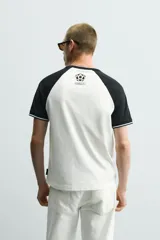 Camiseta de corte regular con diseño color block, cuerpo en color blanco y mangas ranglán en color negro. Presenta cuello redondo, detalles de rib a contraste en los puños y estampado frontal con la leyenda Mexico 70.