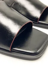 Sandalias negras de cuero con punta cuadrada, dos tiras anchas sobre el empeine y tira con hebilla al tobillo.