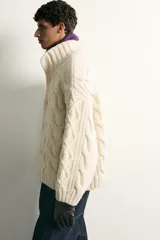 Jersey relaxed fit de punto tejido en hilatura de lana color blanco, con cuello subido, manga larga y acabados en rib. Presenta diseño de trenzas y cierre frontal con botonadura oculta.