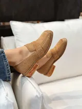 Mocasín de punta cuadrada confeccionado en piel con textura de pelo, color beige tostado, con detalle de antifaz en el empeine y costuras visibles en el borde.