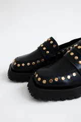 Mocasines de cuero color marrón con suela track negra y tachas doradas.