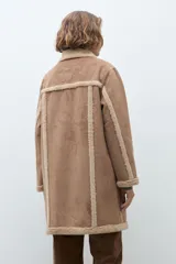 Abrigo de estilo duffle coat en simil gamuza color tostado, con interior y bordes de piel sintética al tono. Presenta cierre frontal mediante alamares de cuero sintético y madera, cuello solapa y mangas largas.