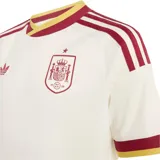 Camiseta de fútbol Adidas de la segunda equipación de la selección de España, color blanco con detalles en bordó y amarillo en cuello, hombros y mangas. Incluye el logo trébol de Adidas y el escudo de la selección bordados en el pecho.