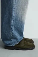 Zapato tipo náutico de hombre, confeccionado en piel con acabado de serraje en color verde oliva. Presenta cordonera con tres pasados, horma redonda y suela track dentada en color negro.
