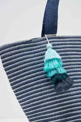 Bolso tipo tote con rayas horizontales en tonos de azul y gris, con asas de hombro azul marino y detalle de borla de hilo en degradé de turquesa.
