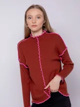 Sweater marrón de punto con cuello alto, manga larga y detalles de volados rosas en cuello, puños y costuras.