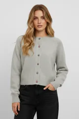 Cardigan de punto gris con cuello redondo, manga larga y cierre frontal con botones de distintos diseños. Presenta puños y ruedo acanalados con un corte holgado.